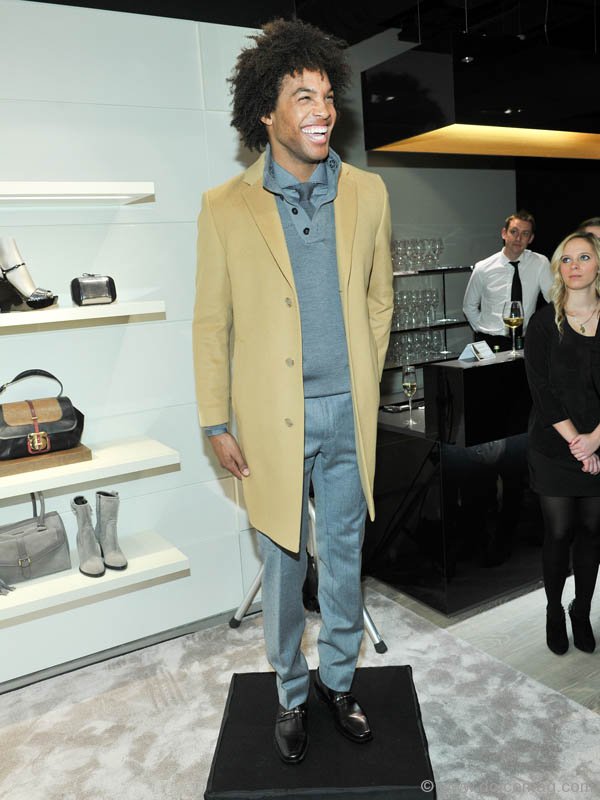 Model in a camel-coloured coat over a grey knit shirt and tie with a light grey flannel trouser and brown loafers, all from the Boss Black collection, Photos By George Pimentel/WireImage