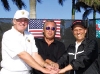 Donald J. Trump, Jim Williams (President of Williams TeleCommunications Corp.) and Mike Milken smiling with hands in a pile in front of the US FLAG.