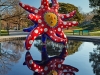 I Want to Fly to the Universe in the reflecting pool features a vivid yellow primordial face, while (right) Hymn of Life – Tulips depicts outsized fibreglass flowers among white lilies | Photo Courtesy Of Yayoi Kusama